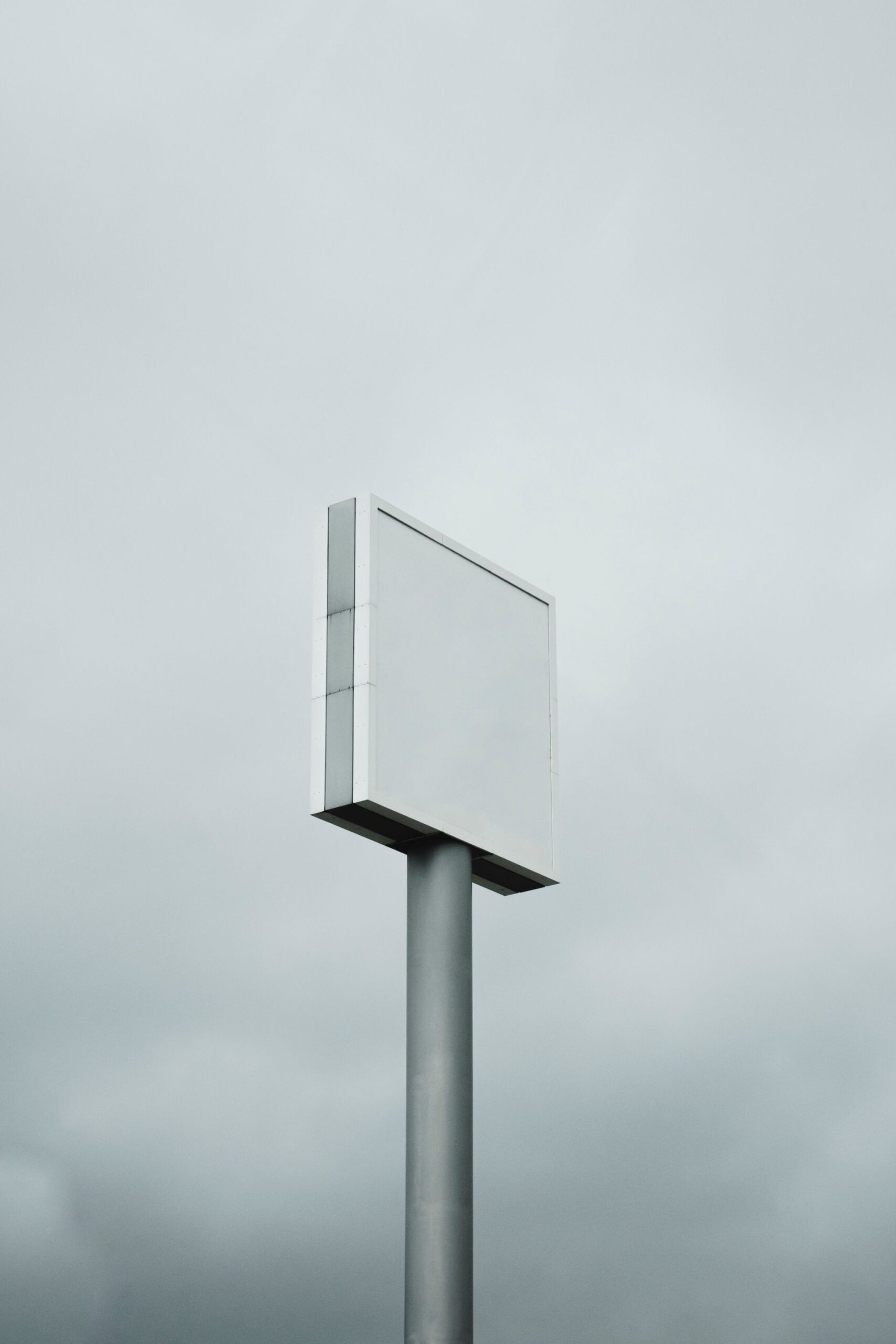Blank sign on a tall pole against a grey sky